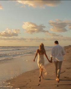 a man and woman walking on the beach holding hands