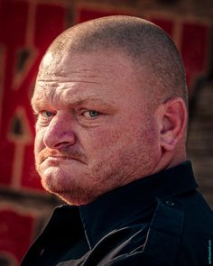 a man with a bald head and blue eyes stares into the distance while wearing a black shirt