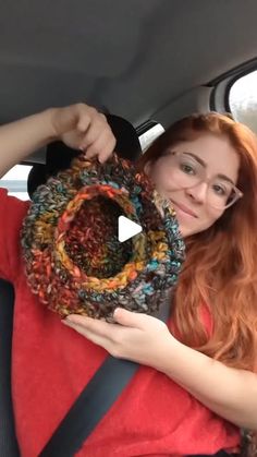 a woman holding up a crocheted scarf in the back seat of a car