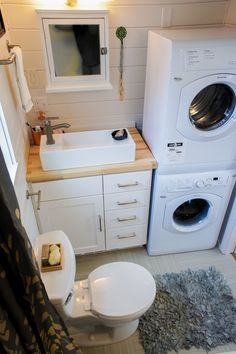 a washer, dryer and toilet in a small bathroom with white cabinets on the walls