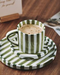 a green and white striped cup sitting on top of a saucer next to a book