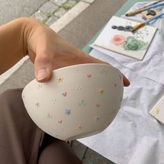 a person is holding a cup in front of their face and painting supplies on the table