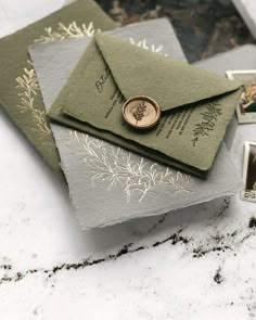 three envelopes with wax stamp on them sitting next to each other, one is green and the other is grey