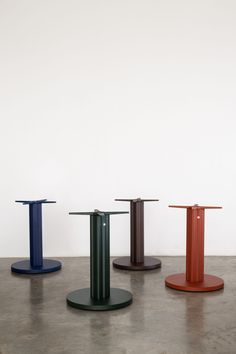 three different colored pedestals sitting on top of a cement floor in front of a white wall