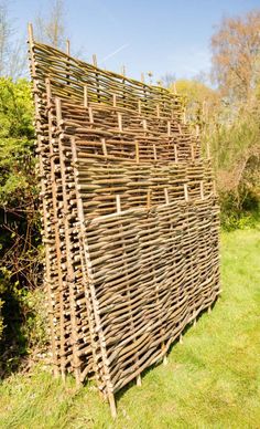 a large wooden structure made out of sticks in the middle of a grassy area with trees and bushes behind it