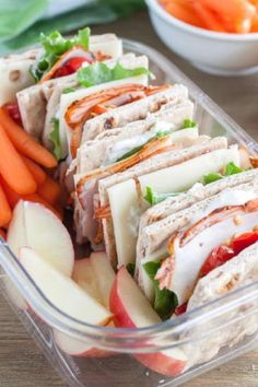 a plastic container filled with sliced up sandwiches next to carrots and celery