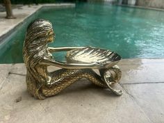 a bronze statue sitting on top of a stone floor next to a pool with water