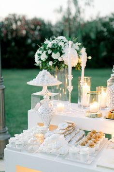 a table topped with lots of desserts and candles on top of a lush green field