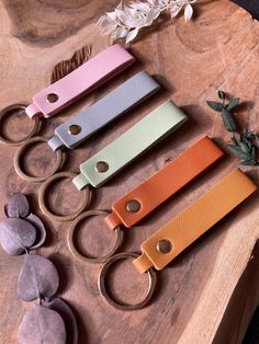 four different colored leather keychains sitting on top of a wooden table next to flowers