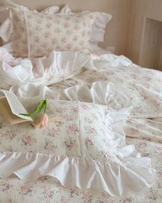 an open book sitting on top of a bed with ruffled sheets and pink flowers