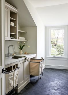 a kitchen with white cabinets and black tile flooring next to an open window that looks out onto the yard