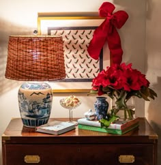 a table topped with vases filled with red flowers next to a painting and lamp