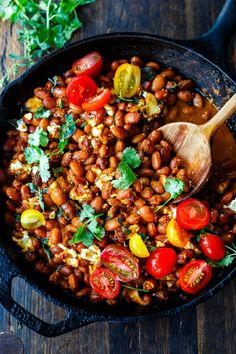 a skillet filled with beans, tomatoes and other vegetables on top of a wooden table