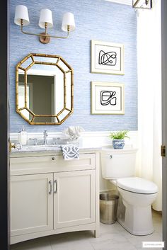 a bathroom with blue wallpaper and white vanity, gold framed mirror above the sink