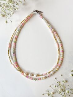 three strand necklace with pink, white and gold beads on a table next to flowers