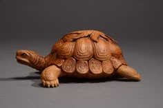 a carved wooden turtle sitting on top of a gray surface with its head turned to the side