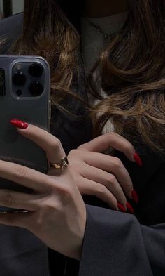 a woman with red nails is holding her cell phone