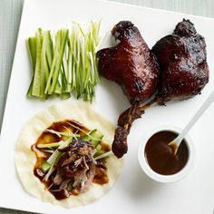 some meat and vegetables on a white plate with sauce in a small bowl next to it