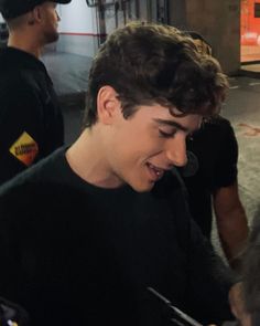 a young man smiles as he looks at his cell phone while standing next to other people