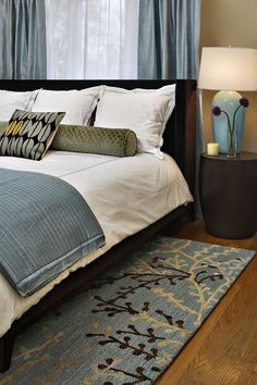 a large bed sitting next to a window with blue curtains and pillows on top of it