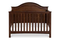 a wooden crib with white sheets on the bottom and side rails, in dark wood