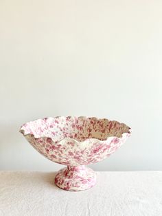 a pink and white flowered bowl sitting on top of a table next to a wall