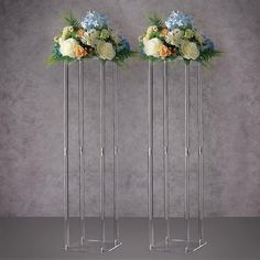 two metal vases with flowers in them on top of a gray table next to each other