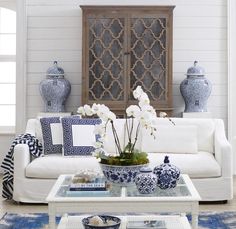 a living room with white furniture and blue vases on the coffee table in front of it