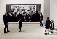 people are looking at an art work on display in a room with white walls and concrete floors