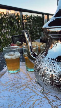 a silver tea pot sitting on top of a table next to two glasses filled with liquid