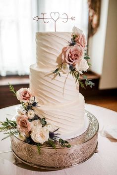 a white wedding cake with pink flowers and greenery sits on a silver platter