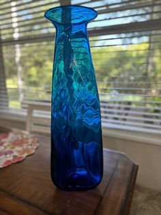 a blue vase sitting on top of a wooden table next to a window with blinds