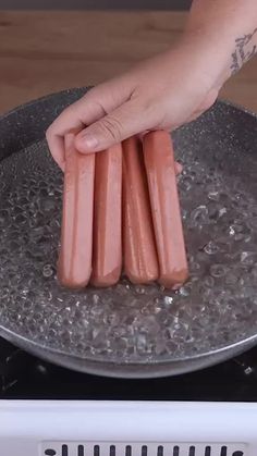 a person is cooking hot dogs in a frying pan