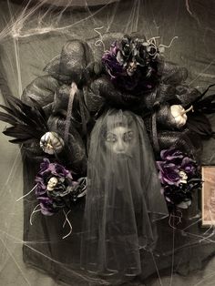 a halloween wreath with black and purple flowers on it, surrounded by fake ghost heads