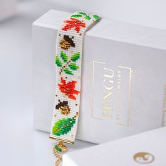 a white box with a beaded bracelet on it next to a gold keychain