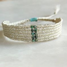 a close up of a bracelet on a white surface with blue beads and green stones