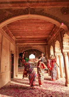 three women in sari walking through an archway with confetti falling from the ceiling