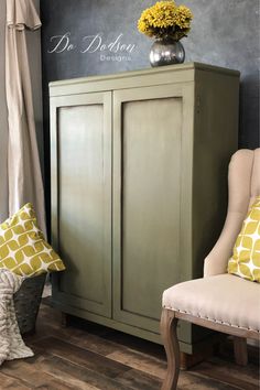 a green cabinet sitting next to a window with yellow pillows on it and a vase filled with flowers