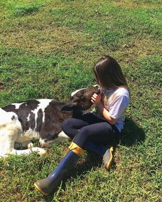 a woman sitting on the grass petting a dog