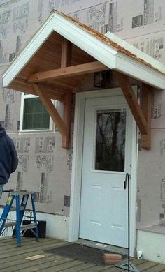 a man standing in front of a white door with a wooden roof over his head