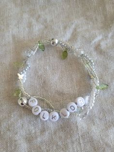 a white beaded bracelet with the word love on it and leaves attached to it