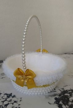 a white basket with pearls and a yellow bow on the handle is sitting on a table