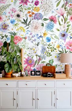 a white dresser topped with lots of drawers next to a wall covered in colorful flowers