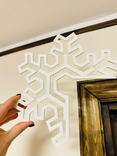 a woman is holding up a snowflake cut out of paper on the wall