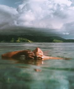 a person floating in the water with their head above the water's surface, under a cloudy sky