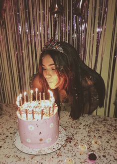 a woman blowing out candles on a birthday cake with pink frosting and sprinkles