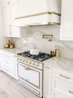 a kitchen with white cabinets and gold trim on the stove top, along with marble counter tops