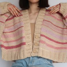 a woman wearing a pink and beige striped cardigan sweater over her shoulders, standing in front of a white wall