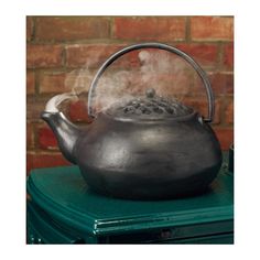 a teapot with steam rising from it on top of a green table next to a brick wall