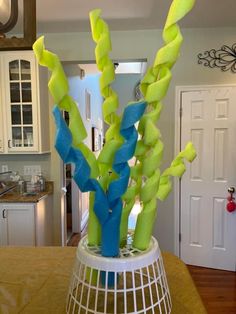 a vase filled with green and blue flowers on top of a wooden table in a kitchen